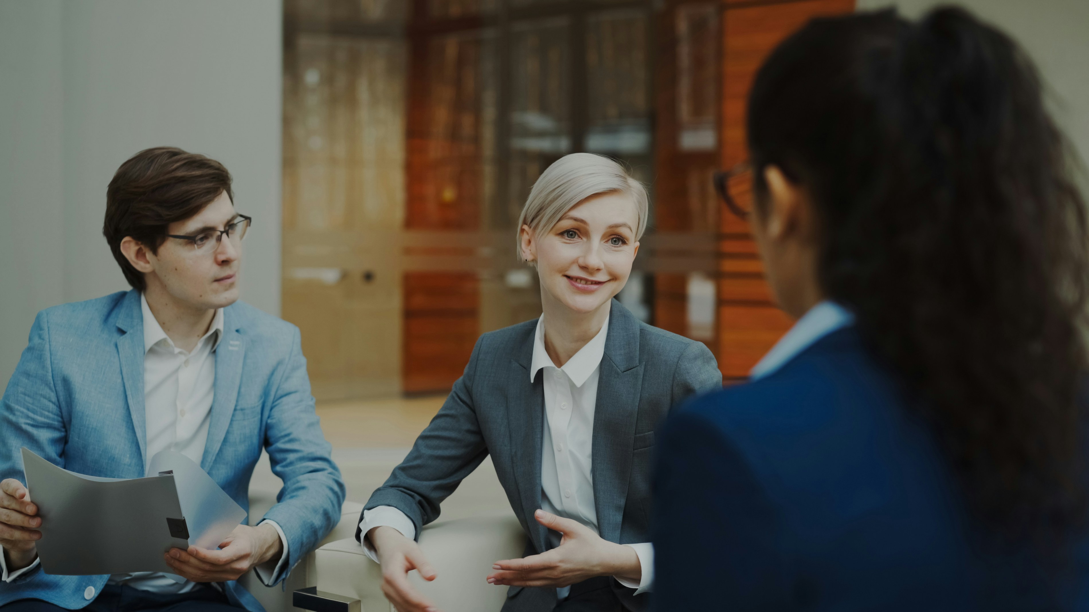Businesswoman talking and duscussing future deal with business partners sitting on couch in modern office center indoors